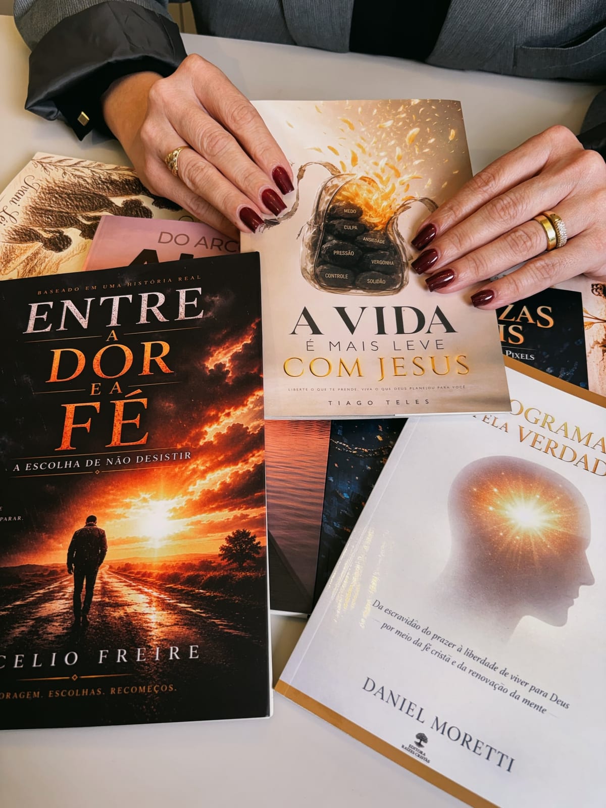 Mãos segurando os livros Entre a Dor e a Fé, A Vida é Mais Leve com Jesus e Reprogramados pela Verdade